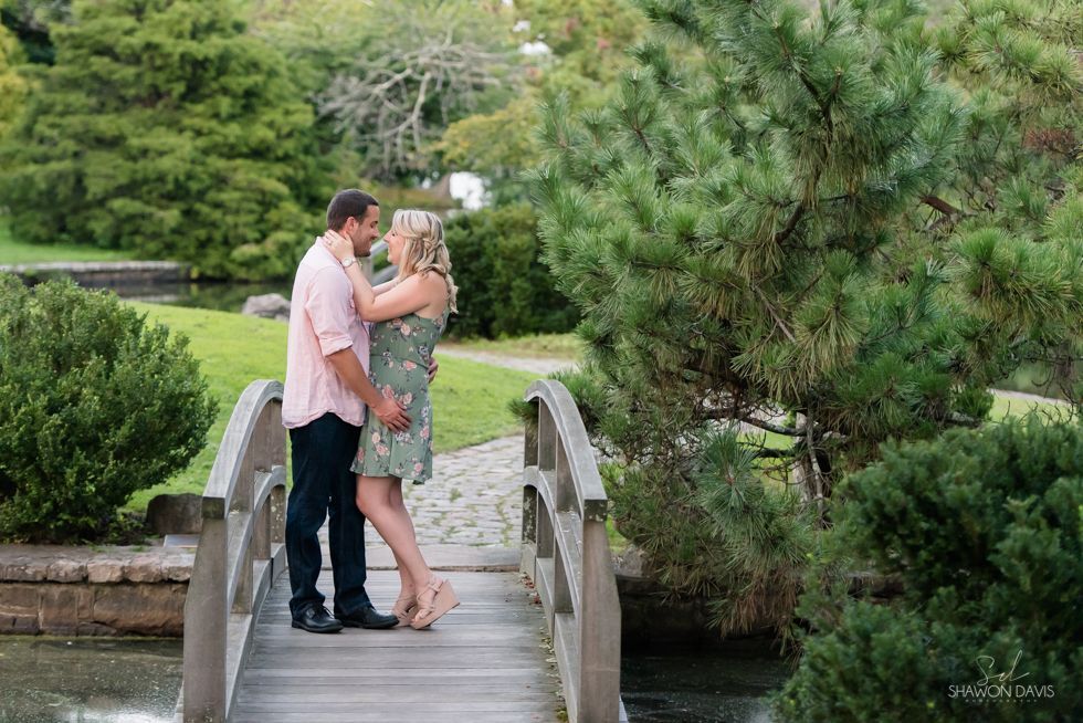 Couple embracing on a small wooden bridge in a lush green garden