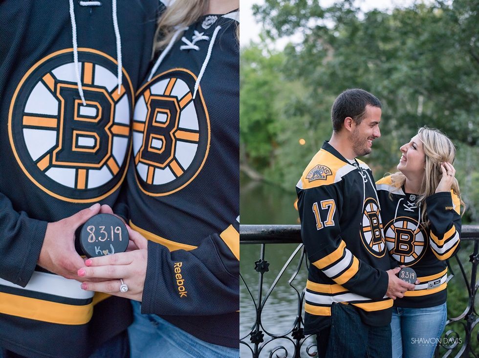 Couple in matching black Boston Bruins jerseys standing by a railing outdoors, smiling and embracing at dusk