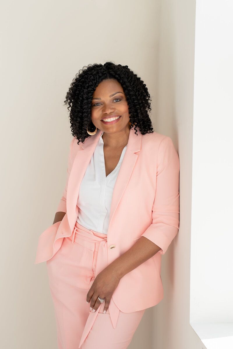 Woman in a pink suit leaning against a wall and smiling