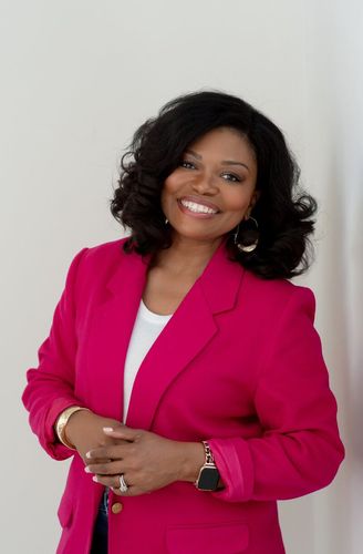 Woman in a bright pink blazer smiling against a plain light background