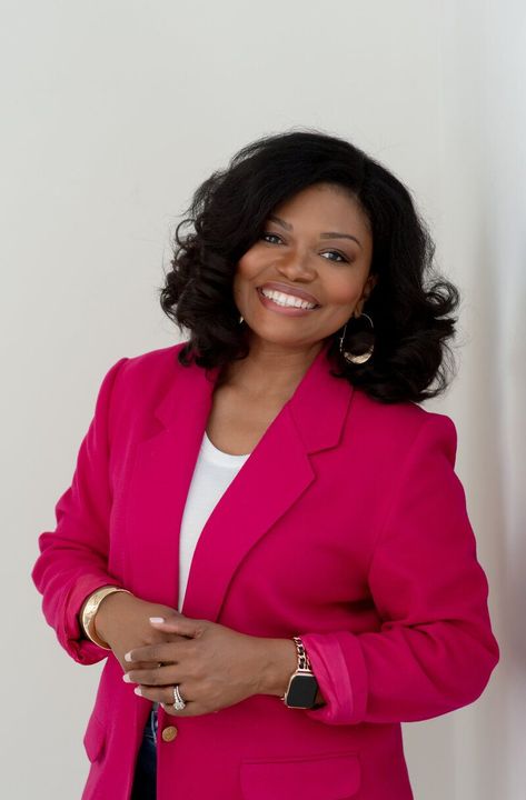 Woman in a bright pink blazer smiling against a plain light background
