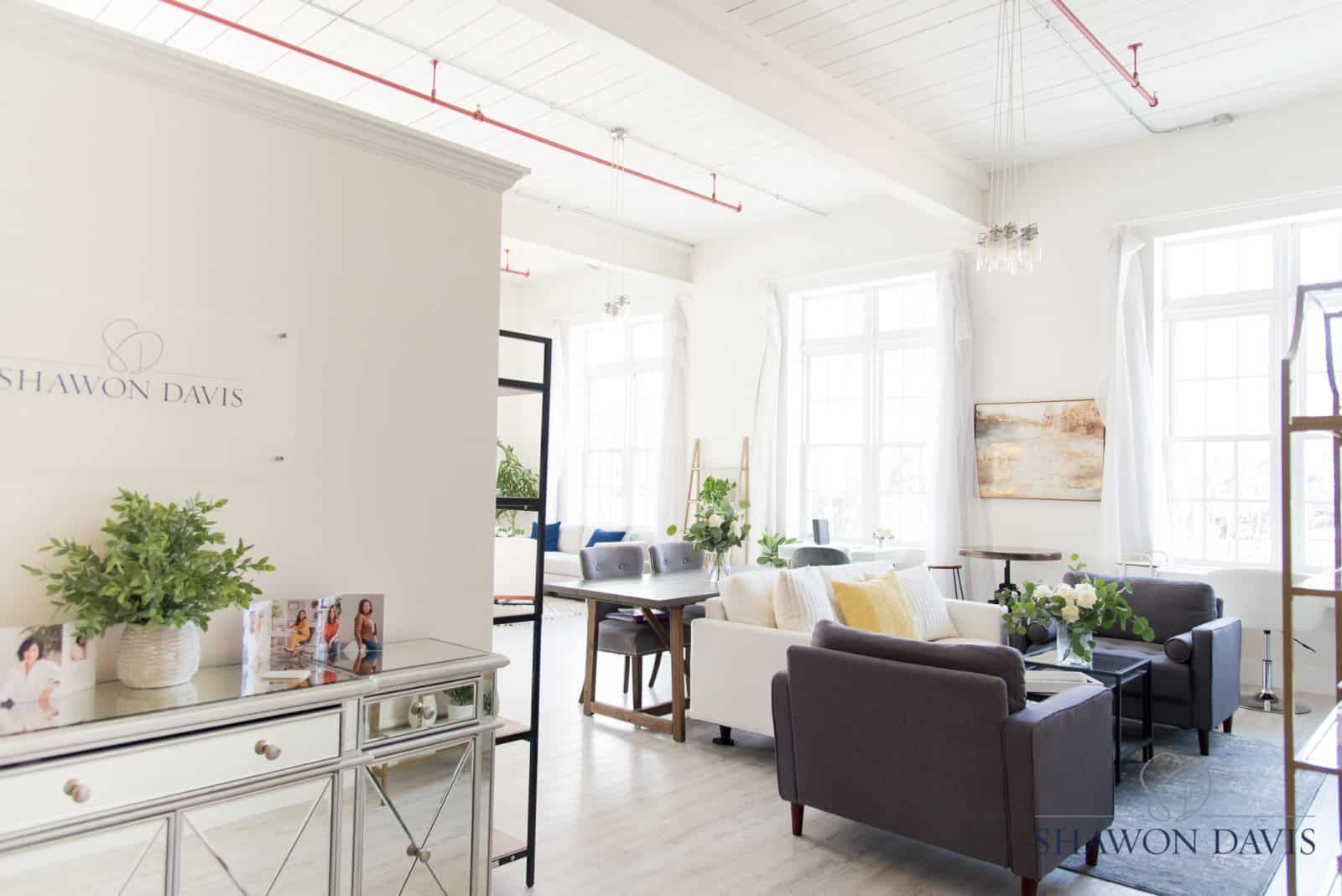 Bright, airy living room with white walls, large windows, and dark sofas around a coffee table