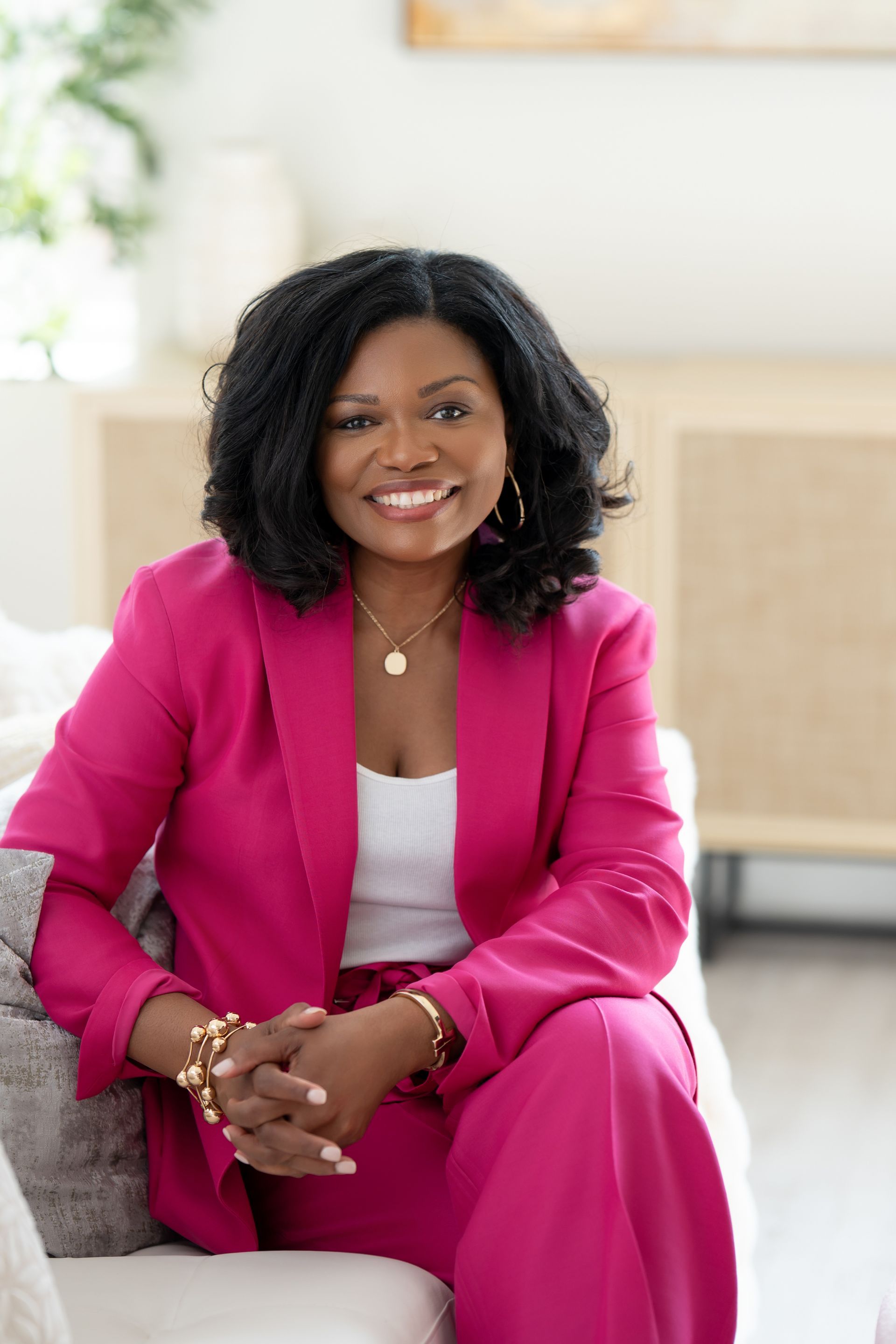 woman sitting on sofa wearing a pink suit and smiling