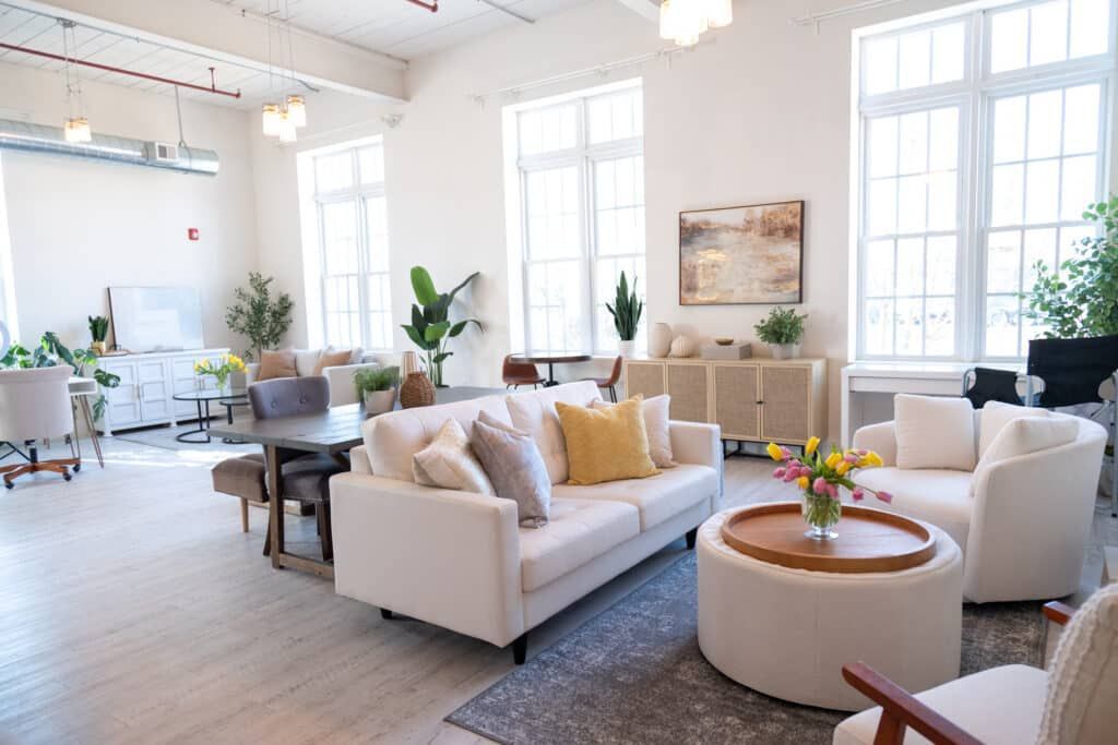 Bright airy living room with white sofas, round coffee table, large windows, and potted plants