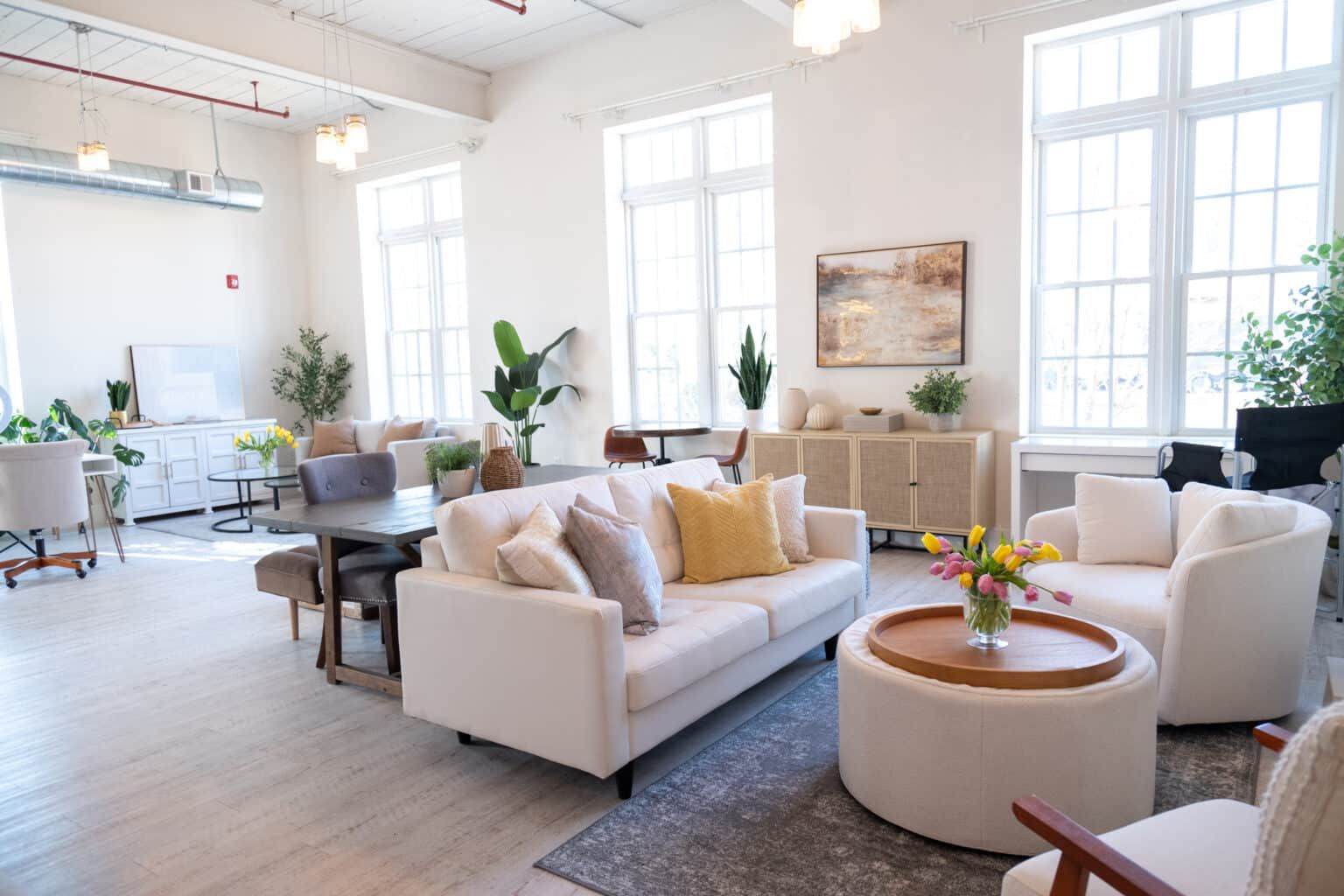 Bright modern living room with white sofas, round coffee table, large windows, and potted plants
