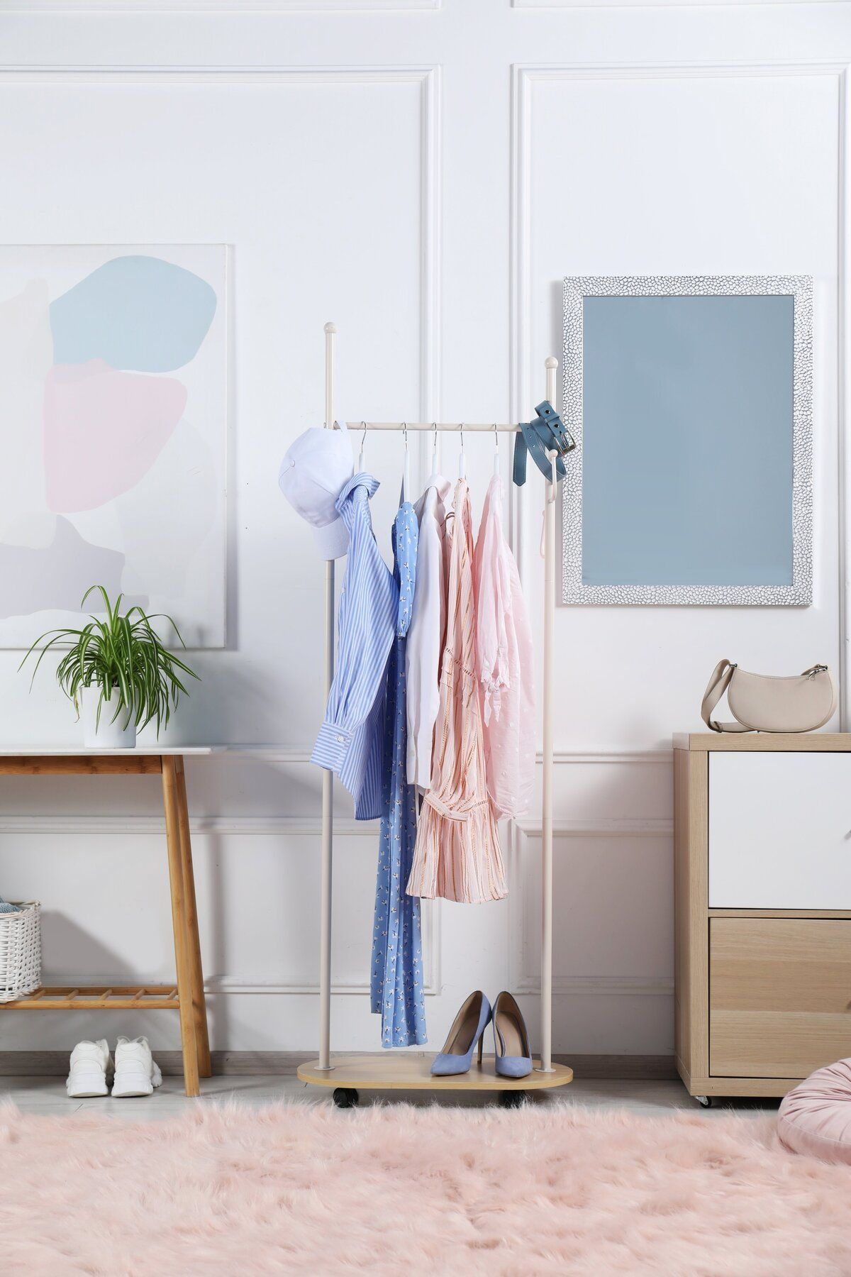 Minimalist bedroom with pastel wall art, clothing rack, small table, dresser, and pink rug