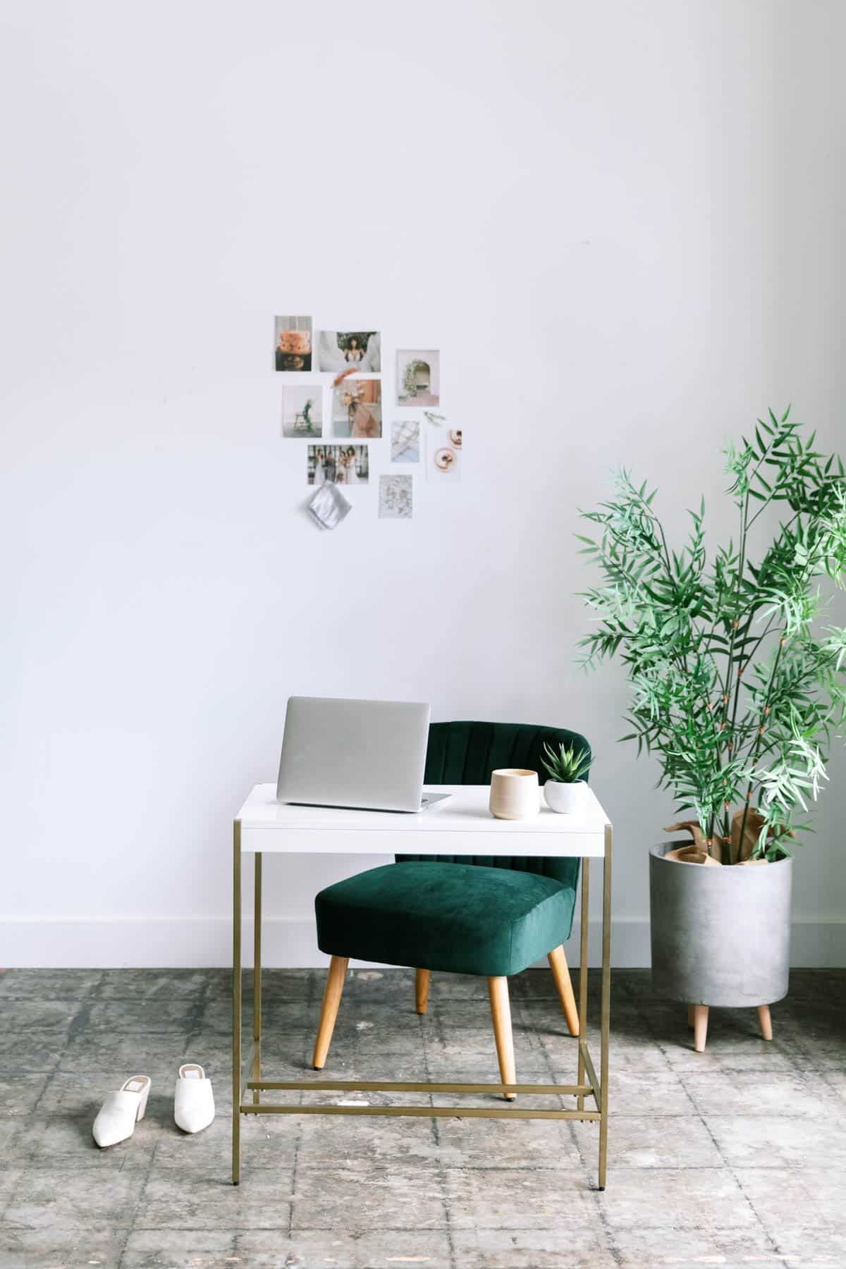 Minimal home office with white desk, green chair, potted plant, and small photo collage on a white wall