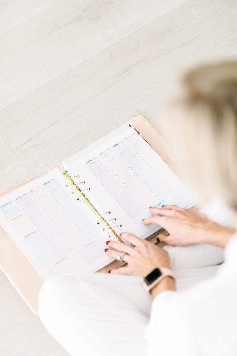 Person writing in a notebook beside an open planner on a white desk