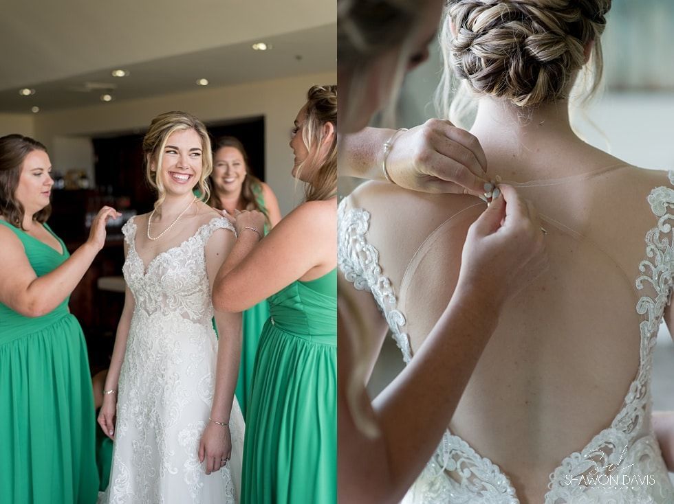 Bridesmaids helping a bride fasten her white lace wedding dress in a bright room