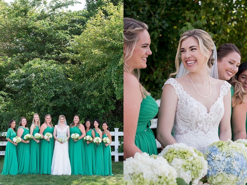 Wedding party in green dresses with bride in lace gown, standing outdoors with bouquets and trees behind them