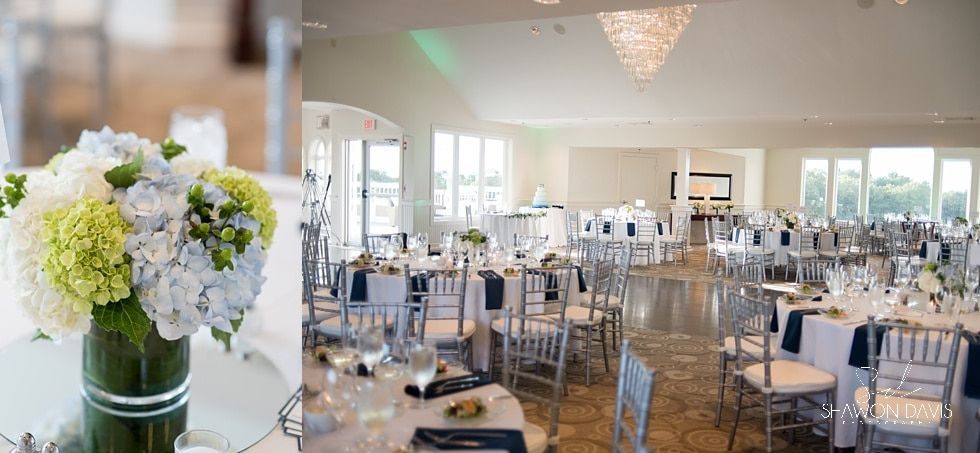 White floral centerpiece on a table beside a bright, elegant banquet hall with clear chairs and set tables.