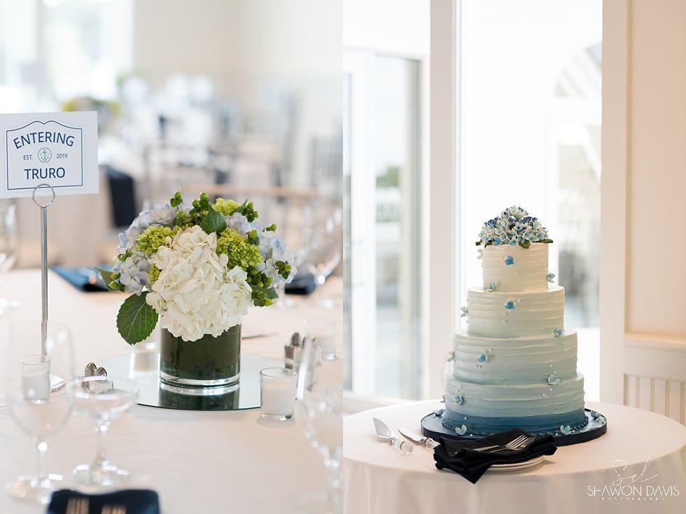Wedding reception table with white floral arrangement, cake, and place card in a bright room