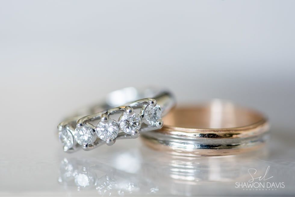 Two diamond rings on a reflective surface, one rose gold band and one silver band with stones