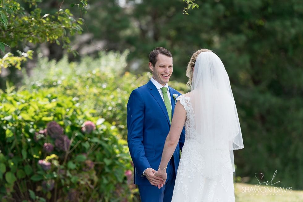 Bride and groom holding hands in a garden, with the groom in a blue suit and the bride in a white veil.