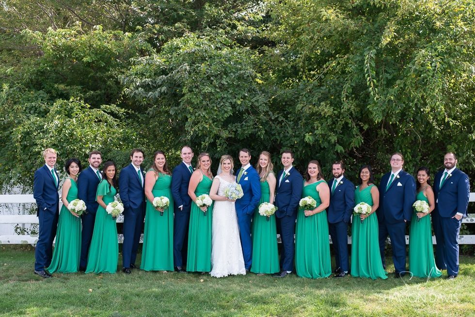 Wedding party posing outdoors in formal teal dresses and dark suits with the bride in white.