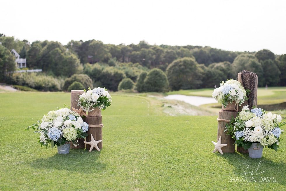 Wedding aisle decorated with white and blue flowers on wooden barrels in a grassy outdoor field