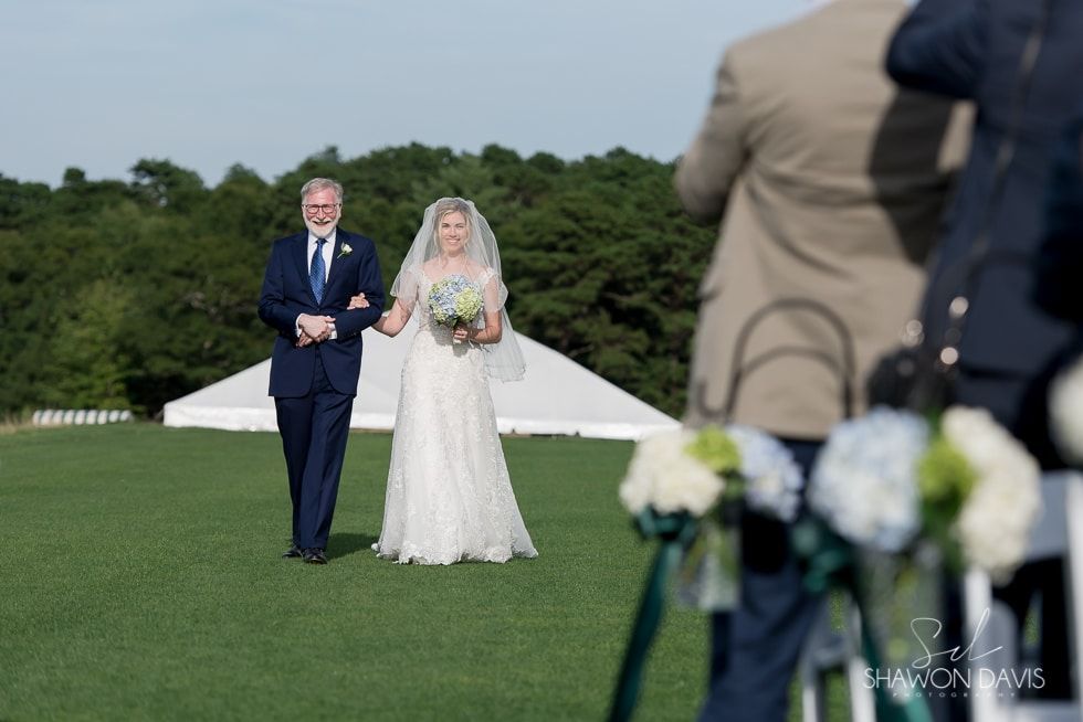 Bride and groom standing outdoors on a lawn at a wedding ceremony, with guests in the foreground.