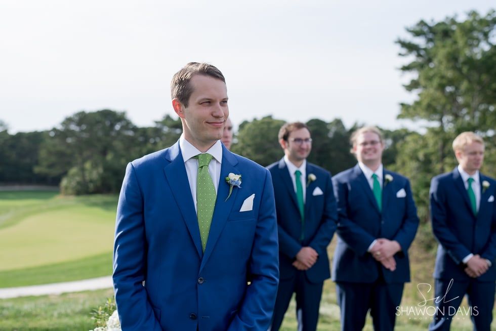 Groom and groomsmen in blue suits standing on a golf course, one man in front looking left.