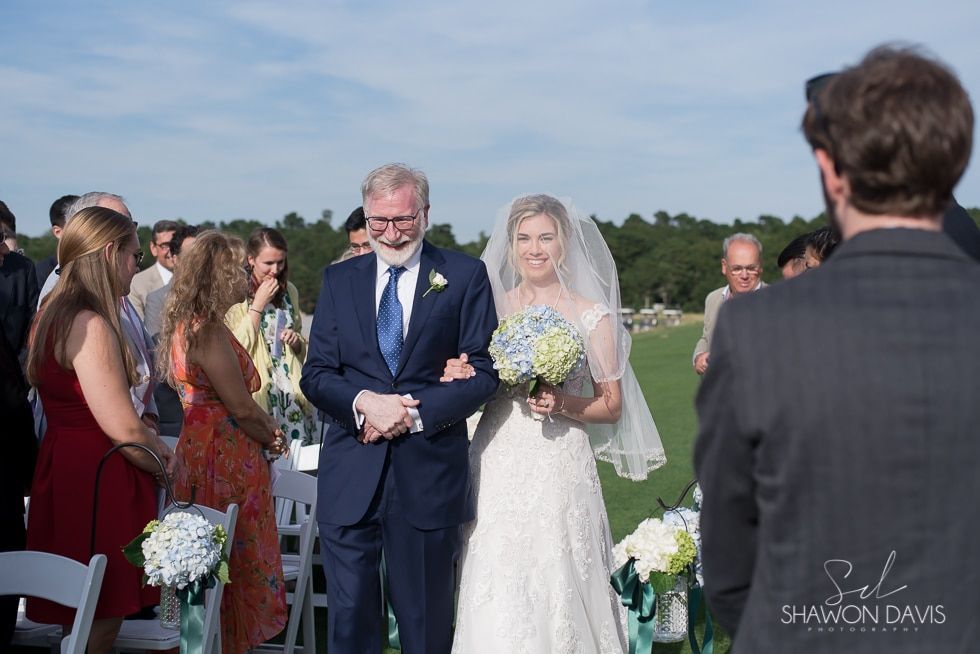 Bride in white dress with bouquet walking arm-in-arm with man in navy suit at outdoor wedding ceremony