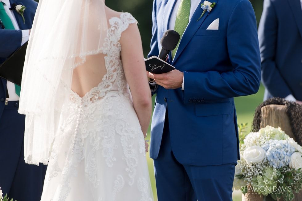 Bride and groom exchanging vows outdoors, with the groom holding a vow book