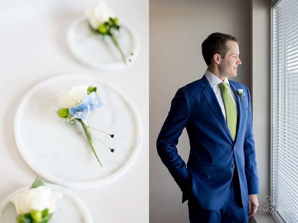 Man in a blue suit and lime tie standing by a window, with floral wall decor in the background
