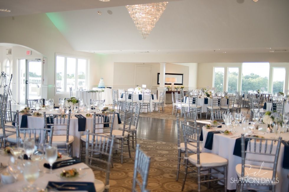 Elegant banquet hall set with round tables, silver chairs, white linens, and glassware before an event.