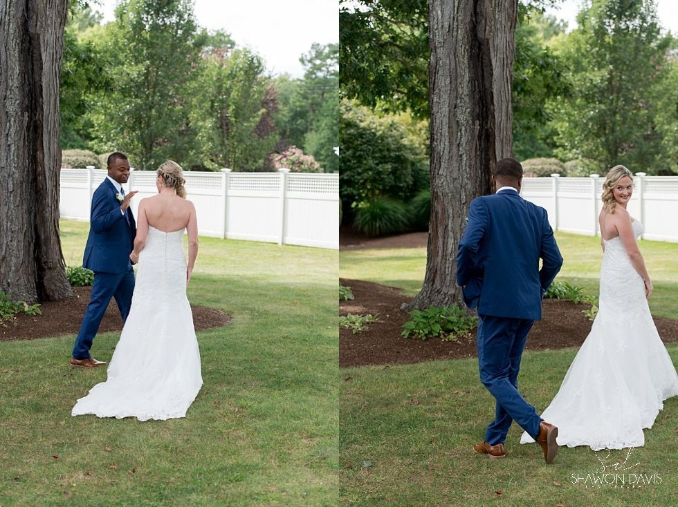 Bride and groom walking apart on a grassy lawn between large trees, with a white fence in the background