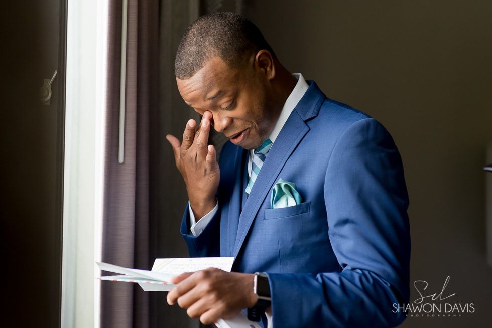 Man in a blue suit reading a card by a window, with a thoughtful expression.