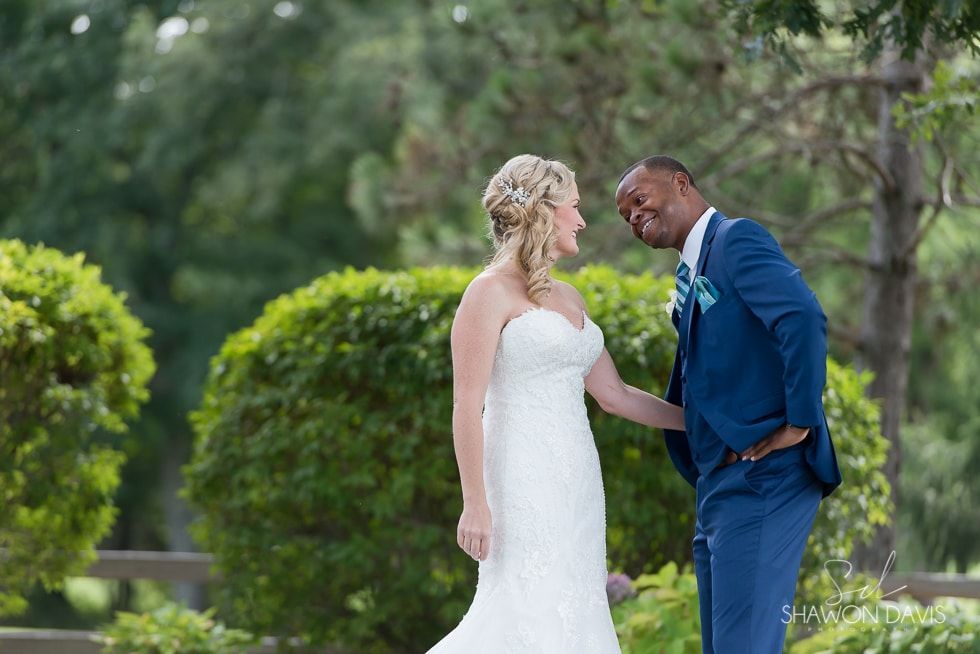 Bride and groom smiling outdoors in a green garden, holding hands during their wedding