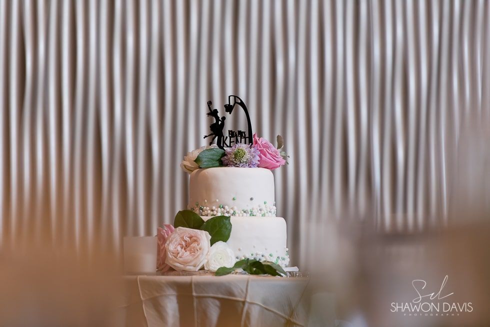 Two-tier white wedding cake with pink and green flowers on a table against a striped backdrop