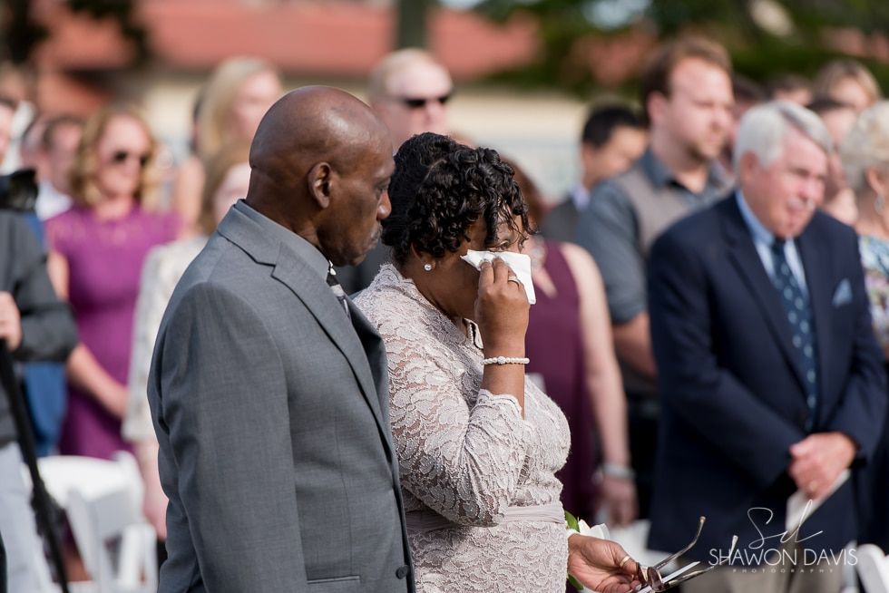 People standing outdoors at a formal event, one person wiping away tears while others look on.