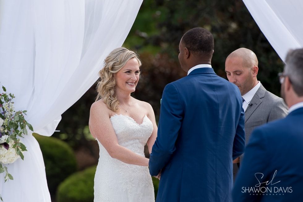 Bride and groom exchanging vows under white drapes at an outdoor wedding ceremony
