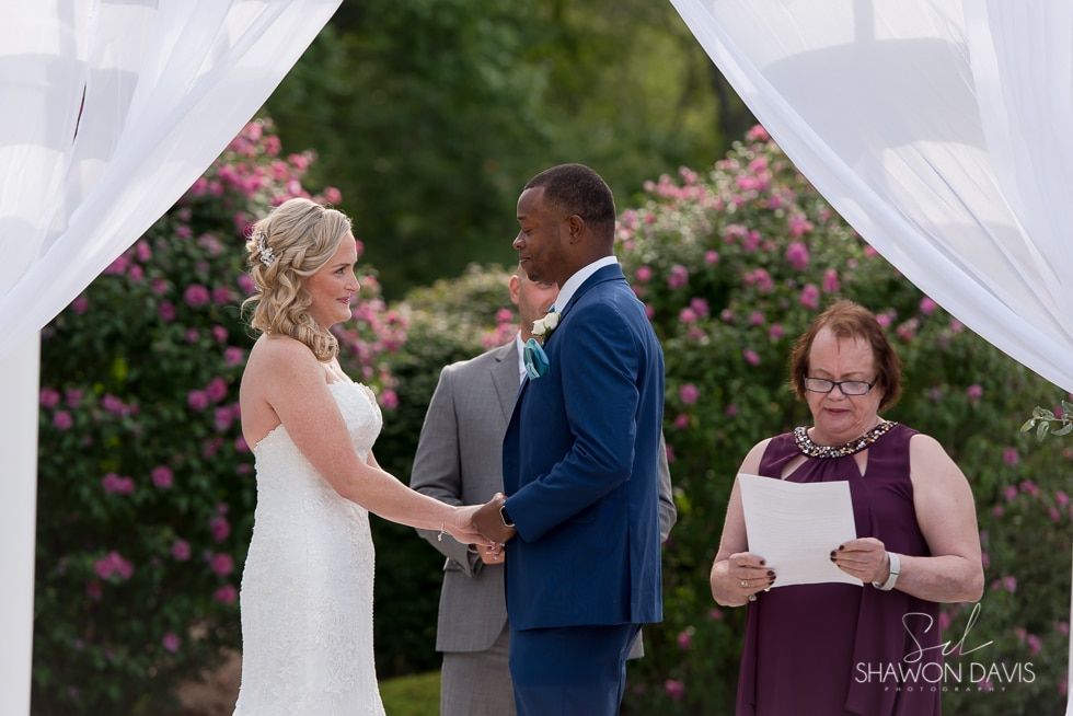 Bride and groom exchanging vows under white drapes at an outdoor wedding ceremony