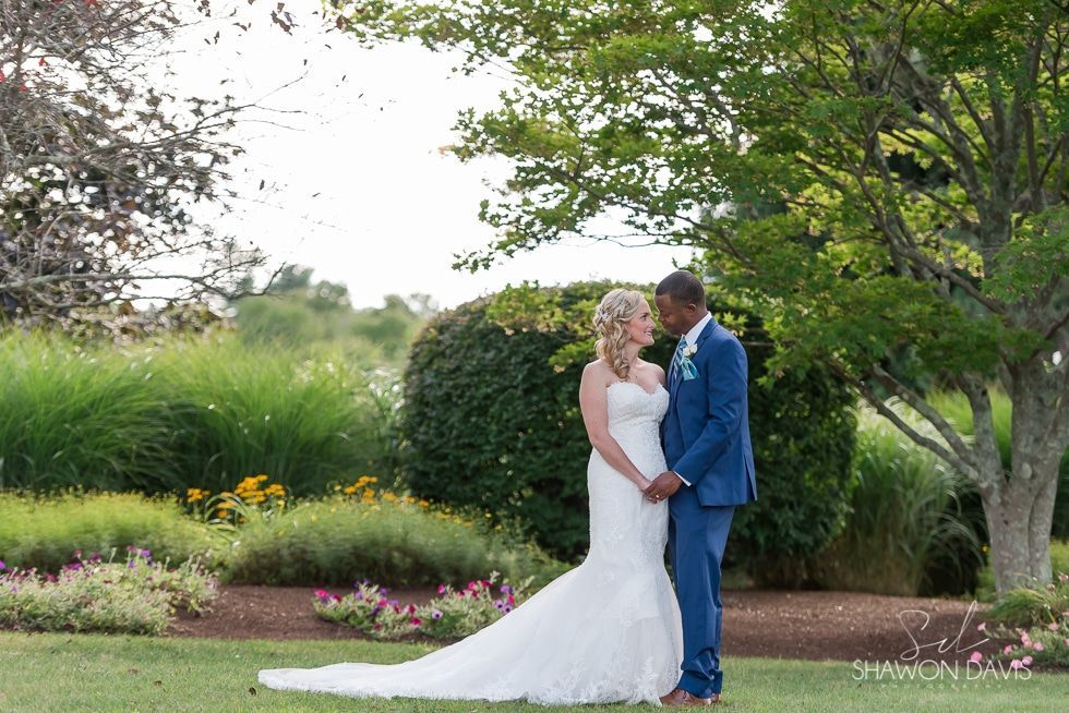 Bride and groom in blue and white wedding attire standing together in a garden.