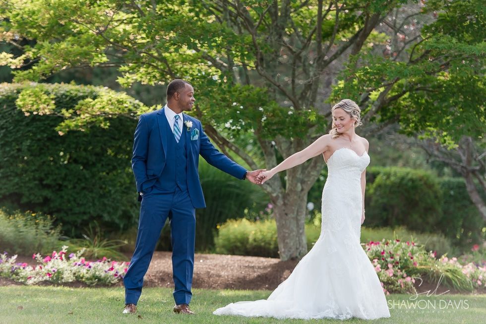 Bride in a white gown and groom in a blue suit holding hands in a garden
