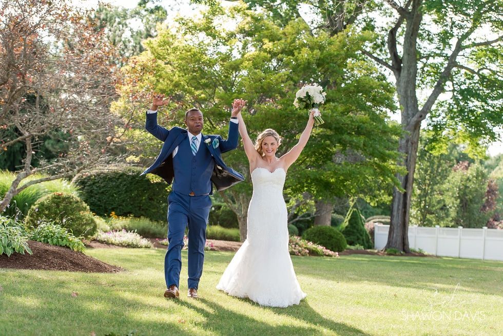 Bride and groom in wedding attire celebrating outdoors with arms raised in a garden lawn