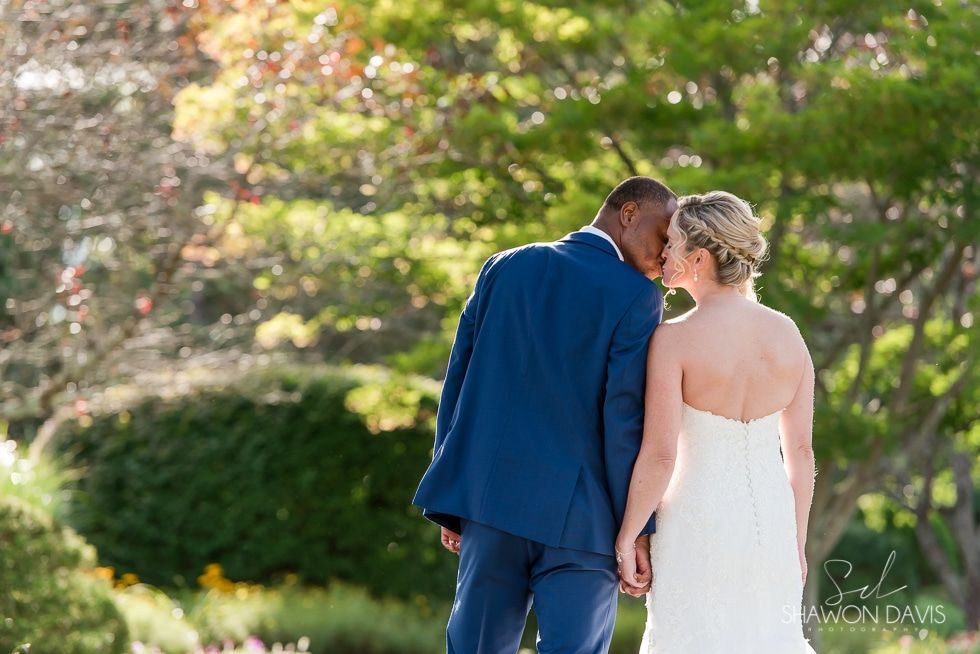 Couple in blue suit and white dress walking hand in hand through a sunlit garden