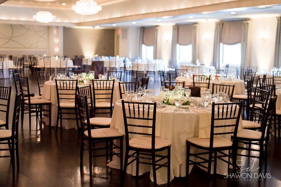 Elegant banquet hall with round, set dining tables, beige chairs, and soft chandelier lighting