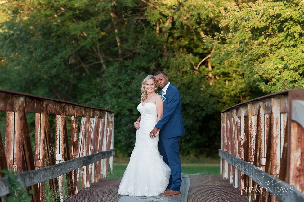 Bride and groom posing on a wooden bridge surrounded by greenery