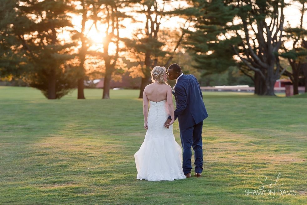 Bride and groom walking hand in hand on a sunlit lawn at sunset