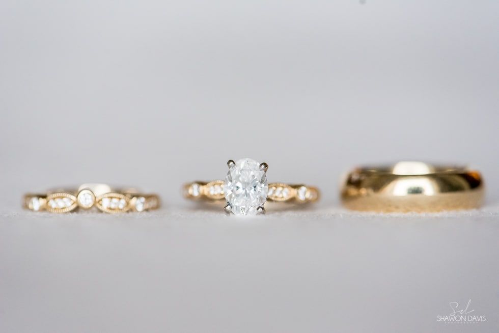 Three gold rings on a light gray surface, with a center ring featuring a large clear gemstone.