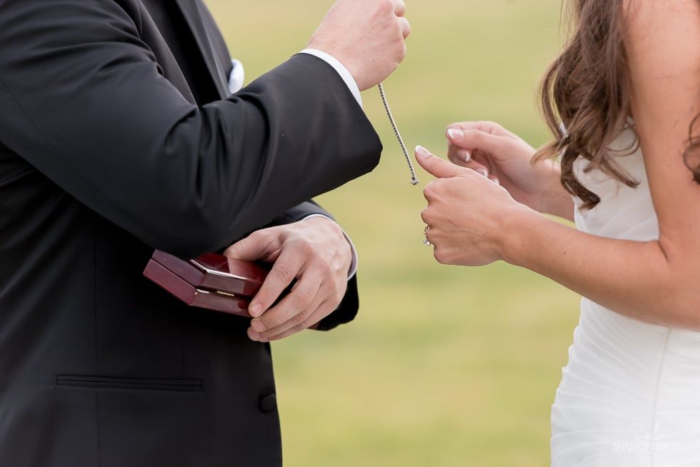 Close-up of a couple exchanging wedding rings outdoors, with a red ring box in hand