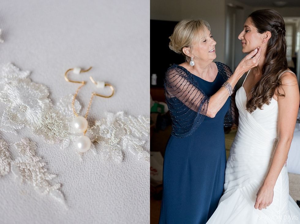 White lace and pearl accessories beside a woman in a blue dress adjusting a bride in a white gown.