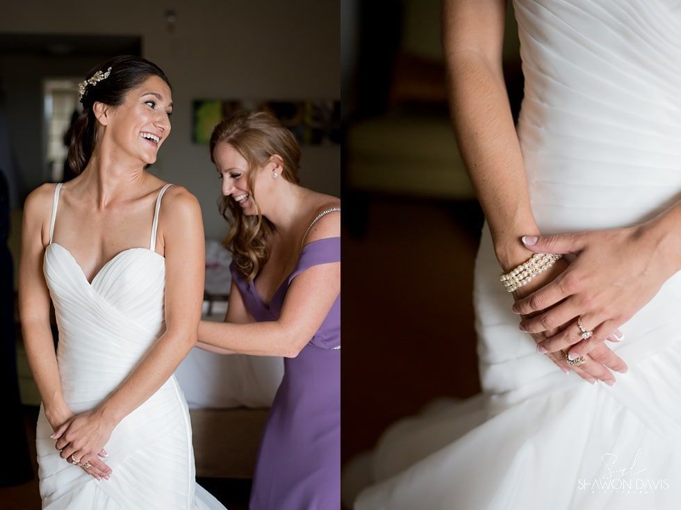 Bride in white dress smiling as attendant fastens her gown, with close-up of hands on dress
