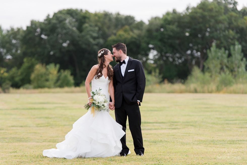 Bride and groom kissing in a grassy field, with trees in the background.
