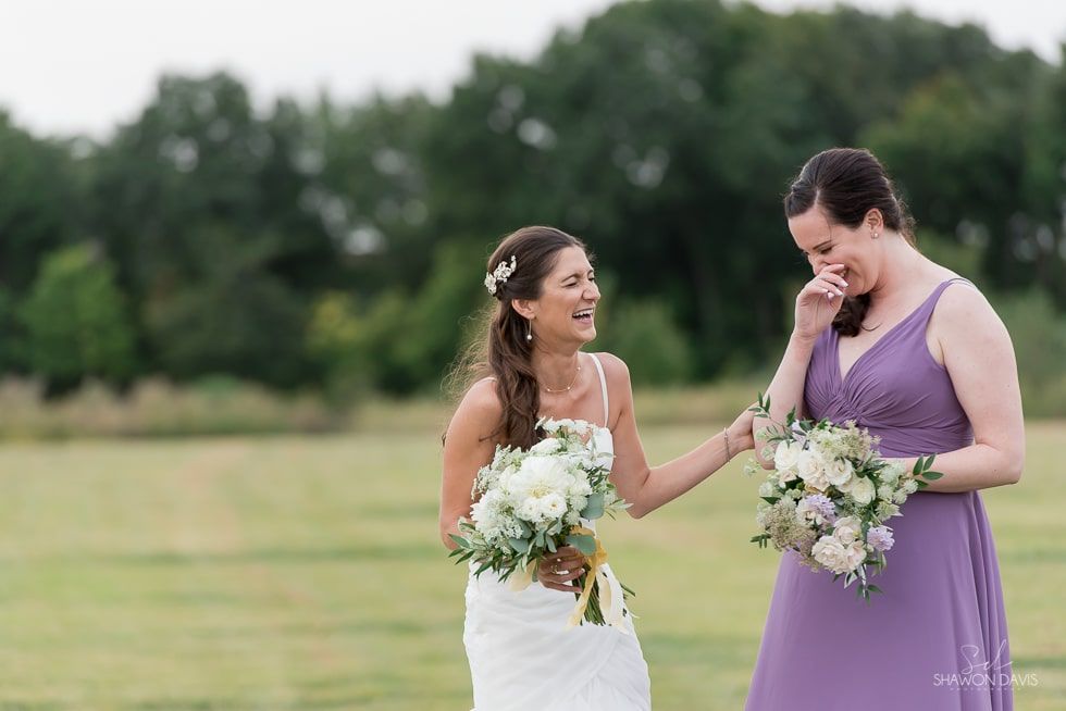 Two women in wedding dresses holding bouquets and smiling in a grassy field