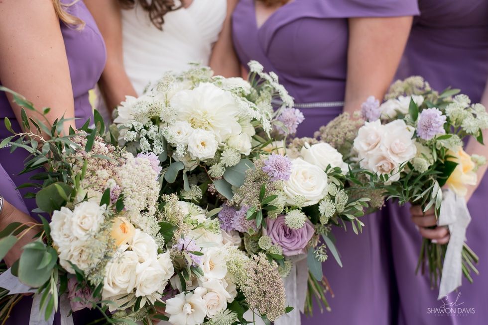 Bridesmaids in lavender dresses holding pastel white and purple floral bouquets