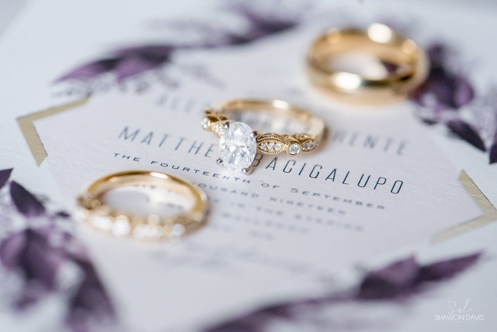 Wedding invitation with gold rings and purple floral accents on a white background