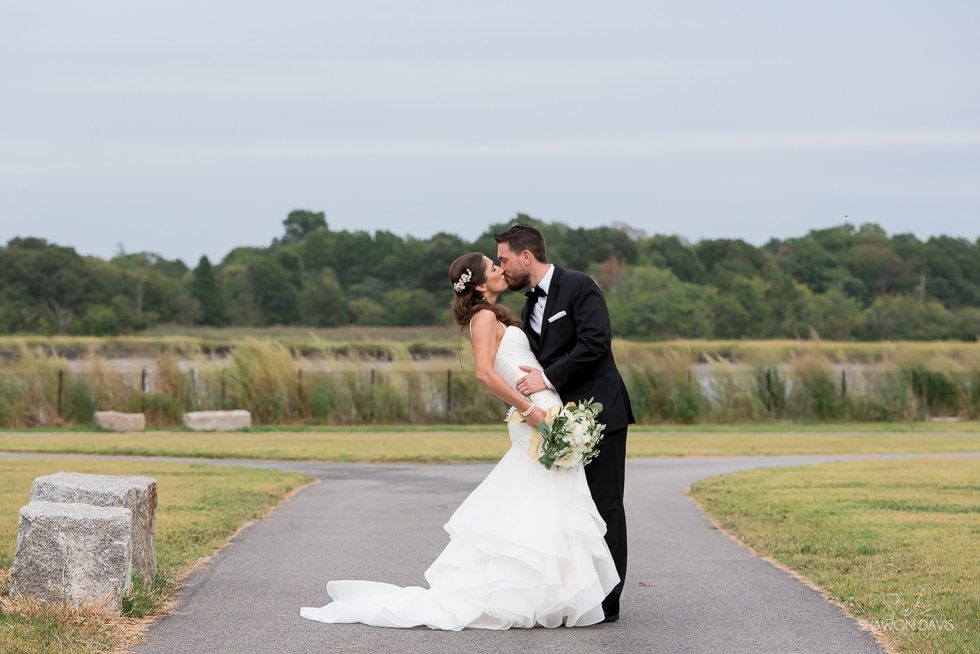 Bride and groom kissing on a paved path in a grassy outdoor landscape