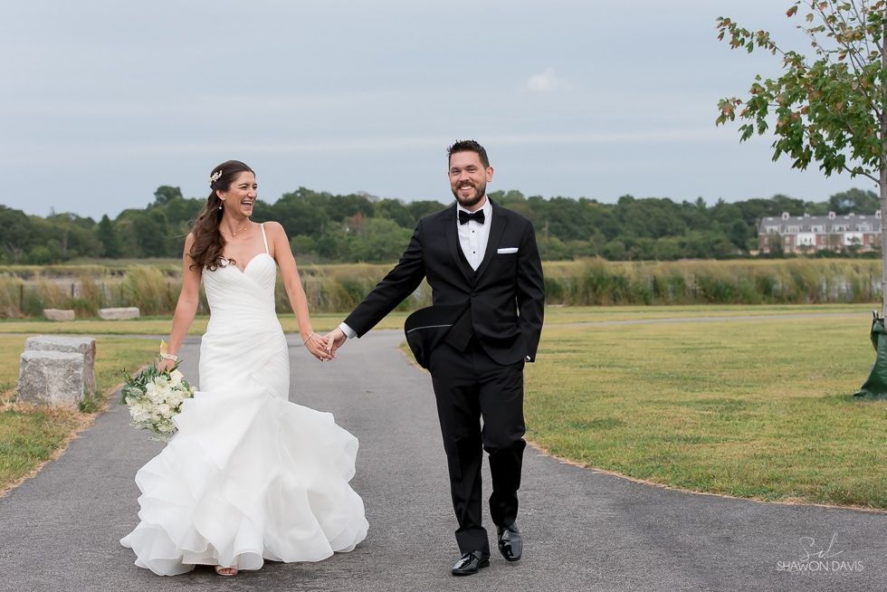 Bride and groom holding hands and walking outdoors in wedding attire on a grassy path